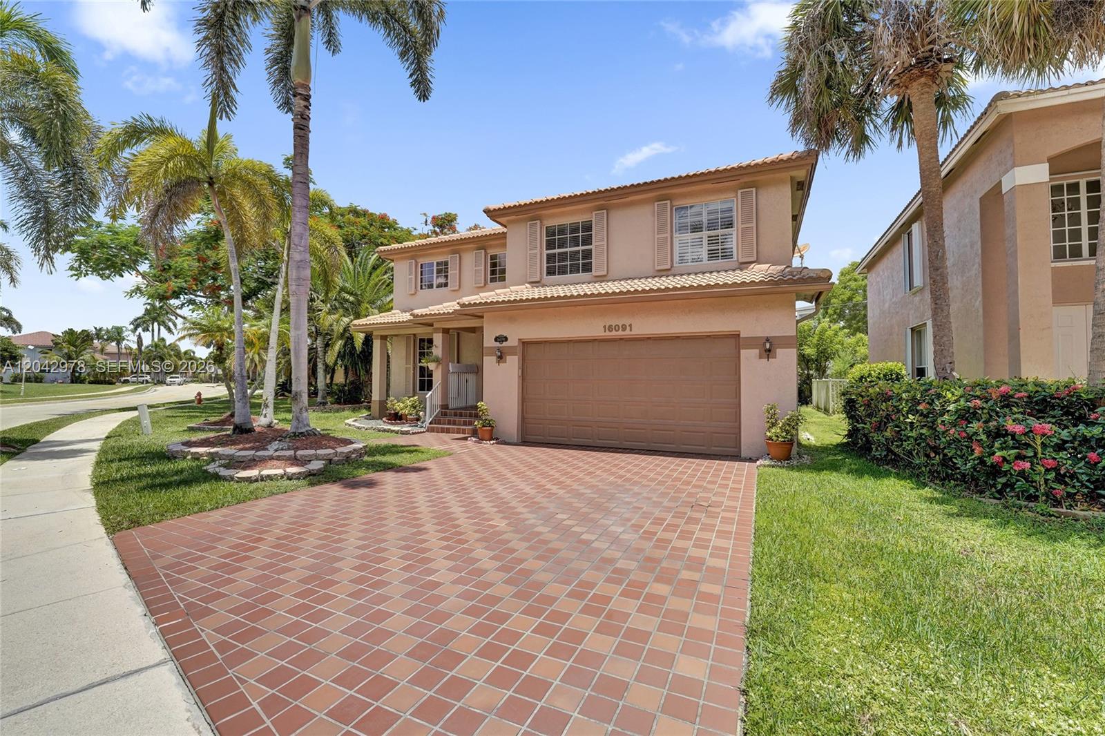 A two-story tan stucco house features a front lawn, palm trees, and a paved driveway — 16091 La Costa Dr, Weston FL 33326, WESTON, FL