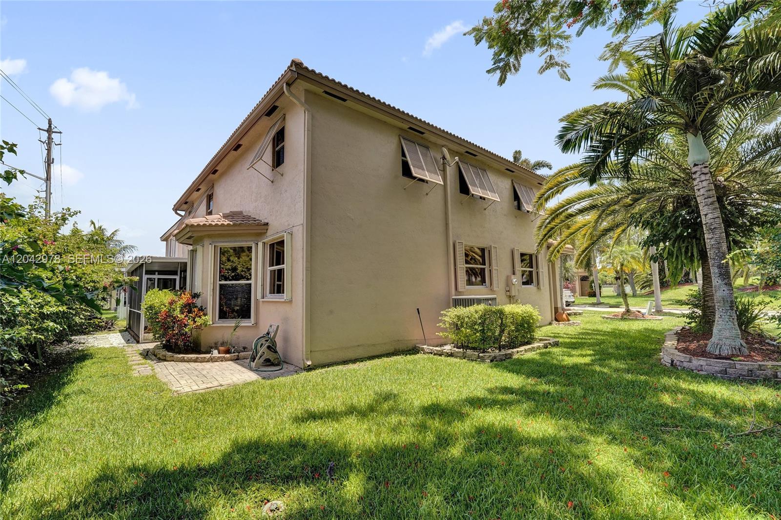 The exterior side of a tan house features shutters, a palm tree, and landscaping — 16091 La Costa Dr, Weston FL 33326, WESTON, FL