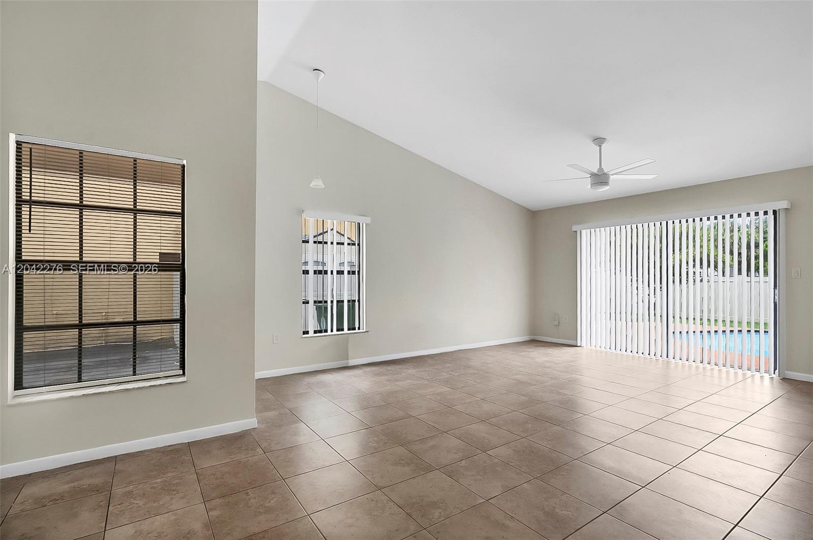 An empty living room features vaulted ceilings, tile flooring, and sliding glass doors to a pool — 681 Thornridge Ave, Davie FL 33325, DAVIE, FL