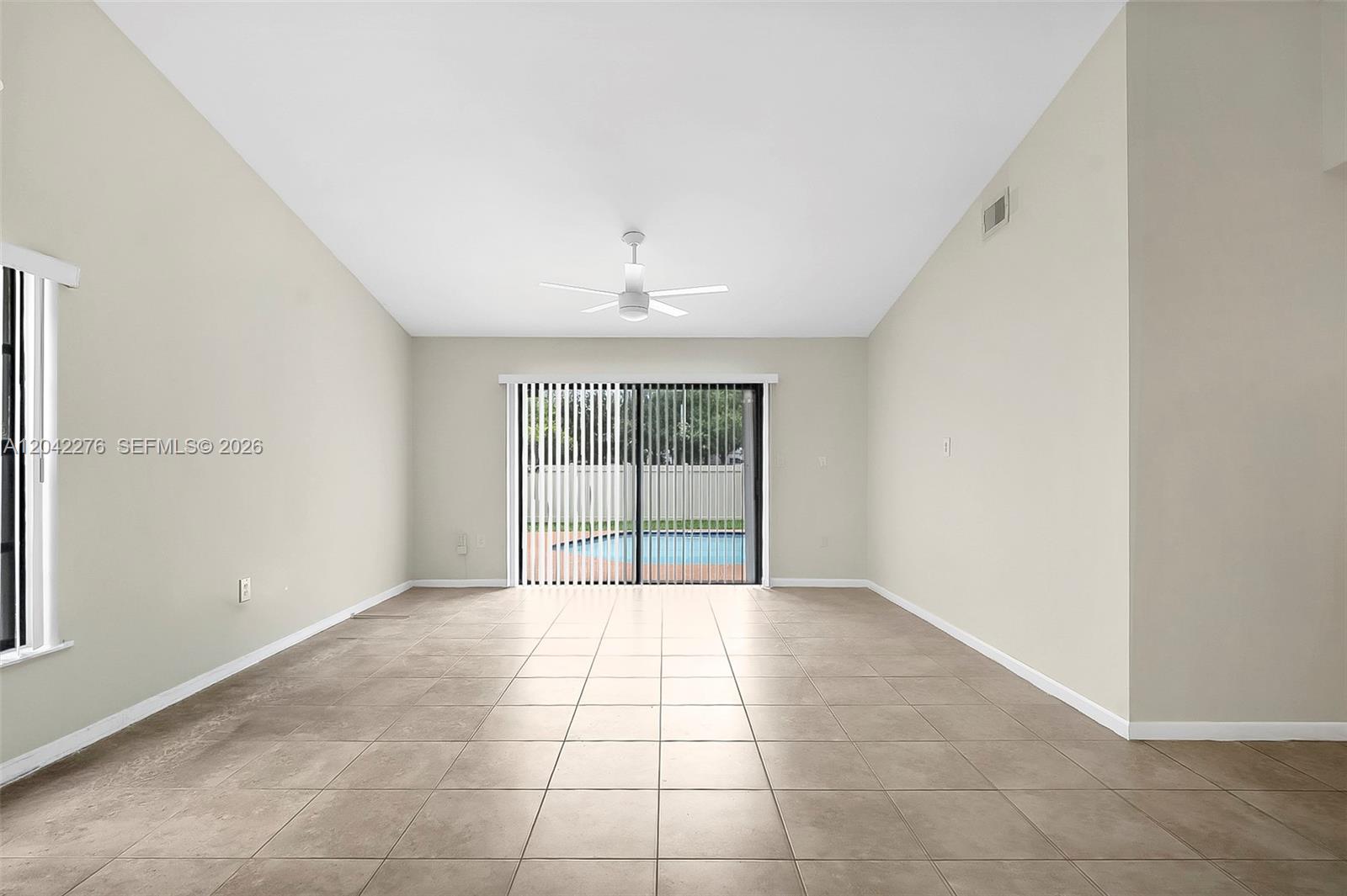 A spacious, empty room features light-colored tile flooring, a vaulted ceiling, and sliding glass doors — 681 Thornridge Ave, Davie FL 33325, DAVIE, FL