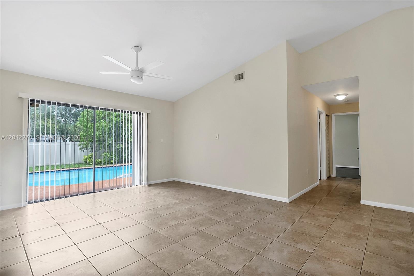 An empty room with beige tile flooring, a vaulted ceiling, and a sliding glass door — 681 Thornridge Ave, Davie FL 33325, DAVIE, FL