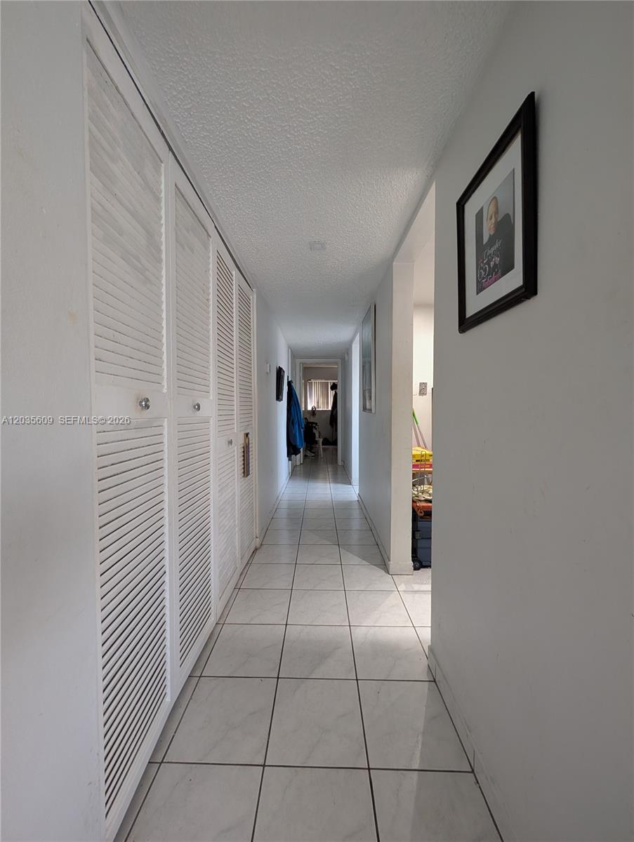 A hallway with white tiled floors and louvered closet doors leads toward a distant room — 19080 NE 3rd Ct # 311, Miami FL 33179, MIAMI, FL