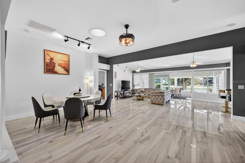 An open-concept dining and living area features light wood-look tile flooring and a dark accent wall — 411 DEL MAR DRIVE, LADY LAKE, FL