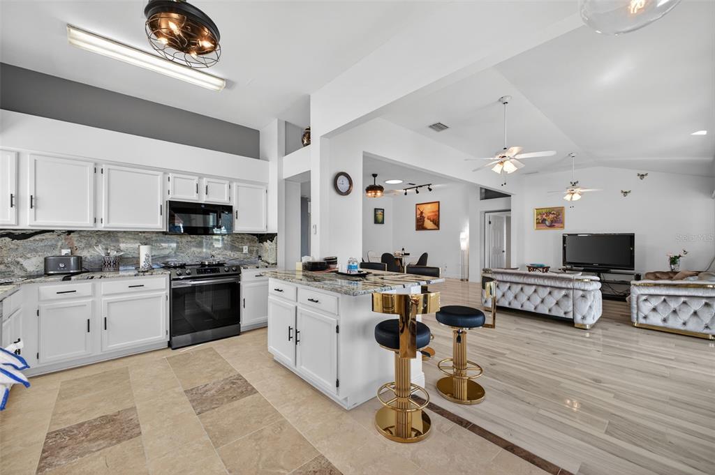 A kitchen with white cabinets and granite countertops opens into a living room with tile floors — 411 DEL MAR DRIVE, LADY LAKE, FL