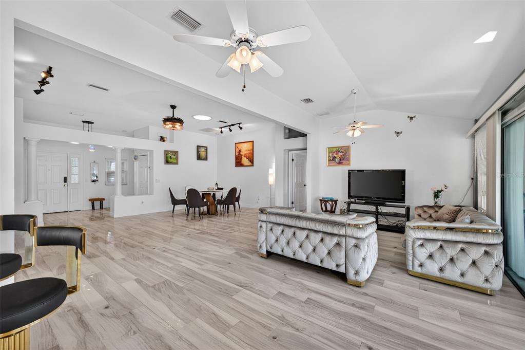 A spacious living and dining area features light wood-look flooring, white walls, and tufted furniture — 411 DEL MAR DRIVE, LADY LAKE, FL