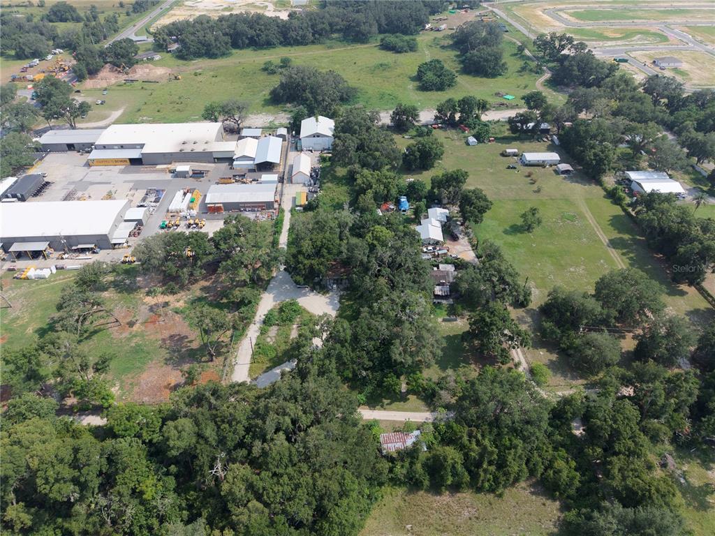 An aerial view shows a commercial warehouse complex adjacent to a wooded residential property — 3350 4TH STREET, OKAHUMPKA, FL