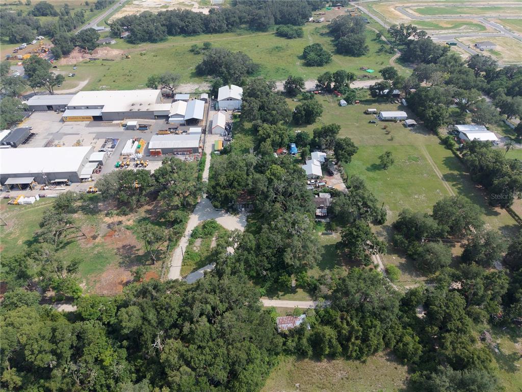 An aerial view shows a rural property with industrial buildings, residential structures, and wooded areas — 3350 4TH STREET, OKAHUMPKA, FL