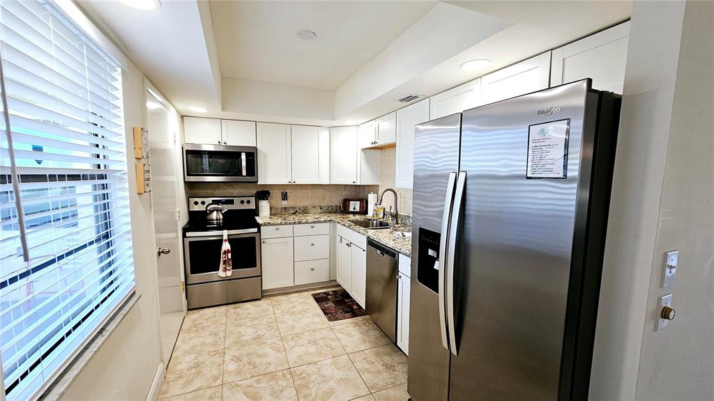 A kitchen features white cabinets, stainless steel appliances, granite countertops, and light-colored tile flooring — 84 BOUNDARY BOULEVARD UNIT 169, ROTONDA WEST, FL