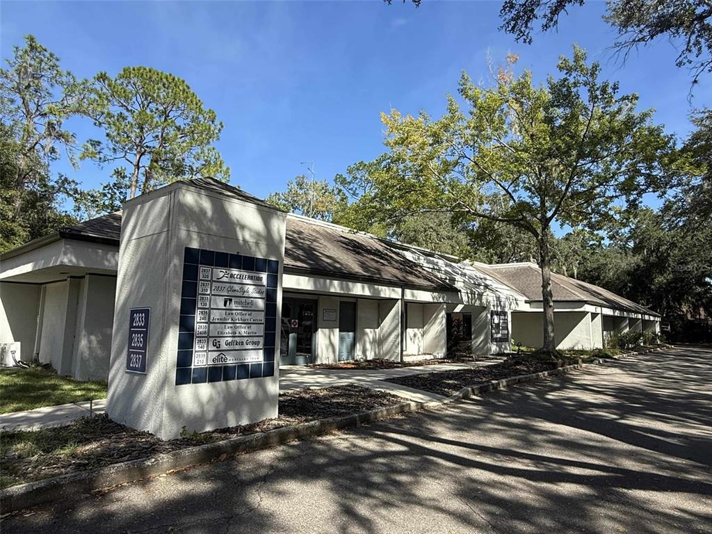 A single-story commercial building features a directory sign on a stucco pillar near the entrance — 2833 NW 41ST STREET UNIT 140 Room B, GAINESVILLE, FL