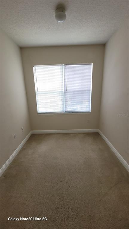 A small, empty room with beige carpet, light-colored walls, and a single window with blinds — 430 SOUTHERN PECAN CIRCLE UNIT 203, WINTER GARDEN, FL