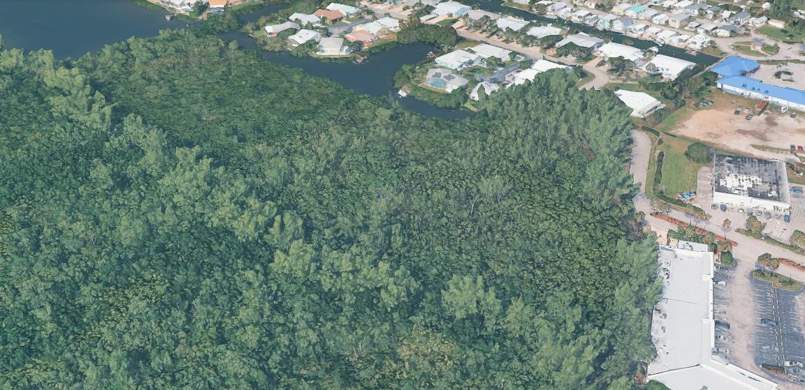 An aerial view shows a dense wooded area adjacent to a residential canal and parking lot — 0 Aqua Ra Drive, Jensen Beach FL 34957, JENSEN BEACH, FL