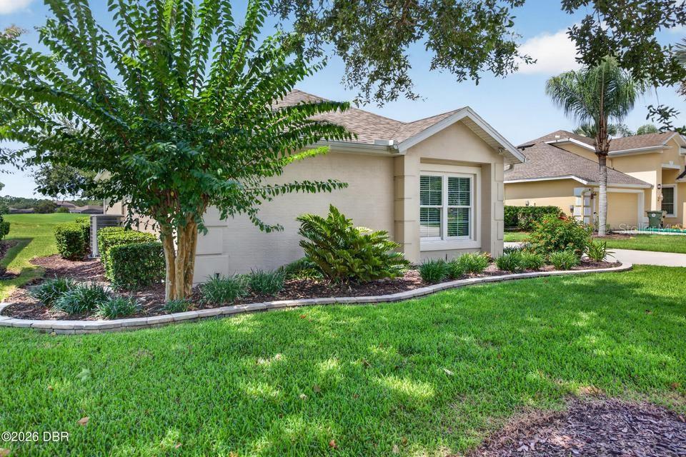 A side view of a beige single-story house with a landscaped yard and a tree — 105 OPAL HILL CIRCLE, DAYTONA BEACH, FL