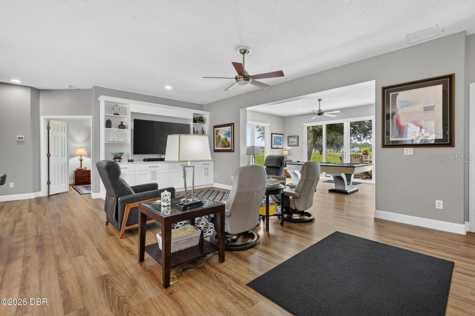 A living room with wood flooring, built-in shelving, a television, and an adjacent game room — 105 OPAL HILL CIRCLE, DAYTONA BEACH, FL