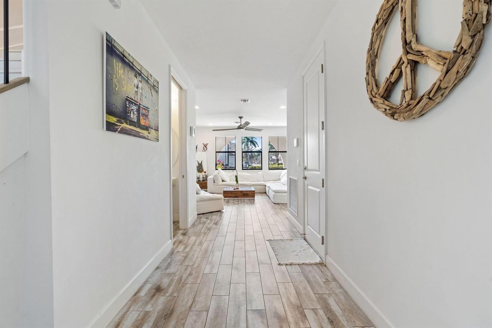 A hallway with wood-look tile flooring leads to a living room with a white sofa — 12512 NW 32 Manor # 3, Sunrise FL 33323, SUNRISE, FL