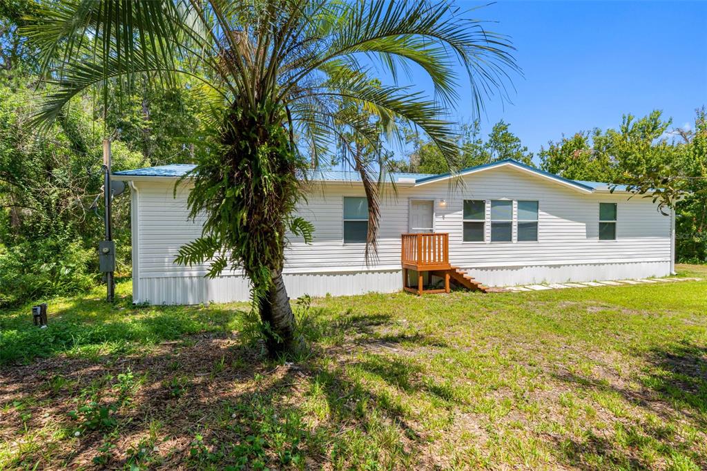 A single-story manufactured home with white siding, a blue metal roof, and a wooden porch — 6847 WOODSMAN DRIVE, WESLEY CHAPEL, FL