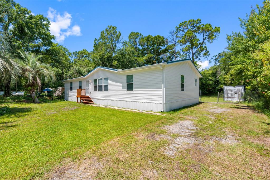 A white single-wide manufactured home sits on a grassy lot with a small wooden deck — 6847 WOODSMAN DRIVE, WESLEY CHAPEL, FL