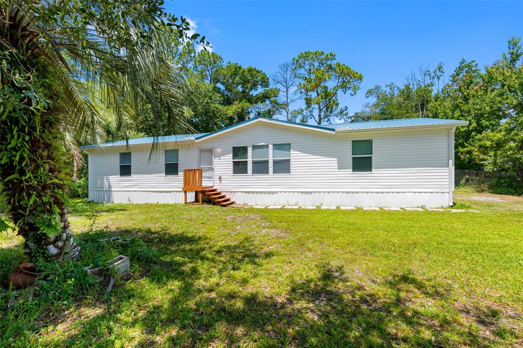A single-story manufactured home with white siding and a blue metal roof — 6847 WOODSMAN DRIVE, WESLEY CHAPEL, FL