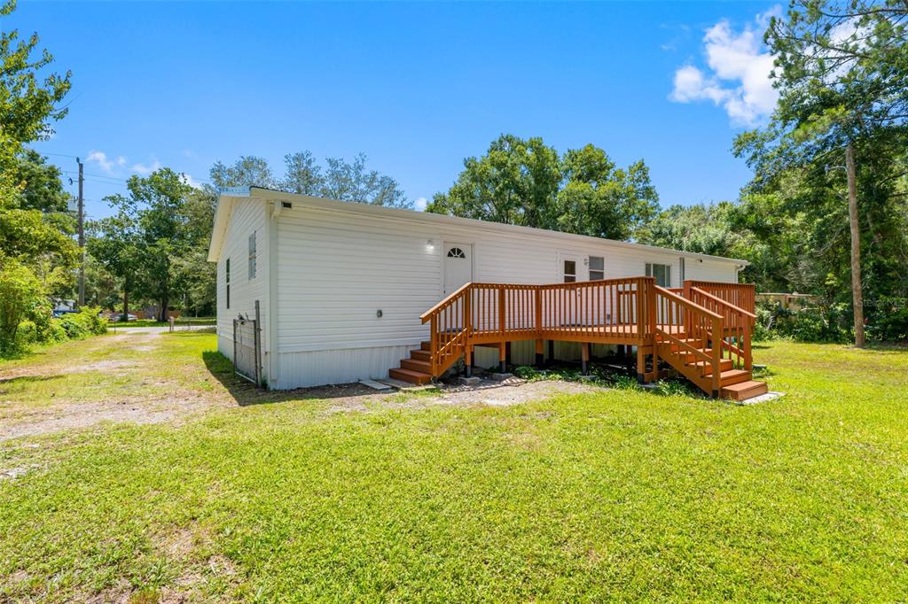 A white mobile home features a wooden deck with stairs in a grassy yard — 6847 WOODSMAN DRIVE, WESLEY CHAPEL, FL