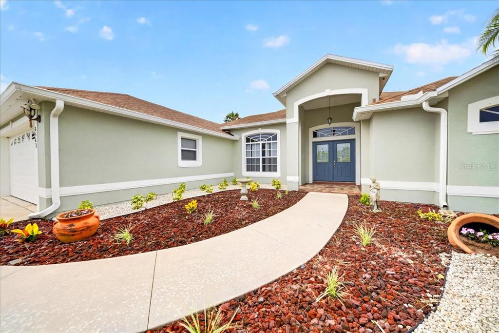 A light green house exterior features a curved concrete walkway leading to a blue front door — 6463 FLORA VISTA PLACE, COCOA, FL