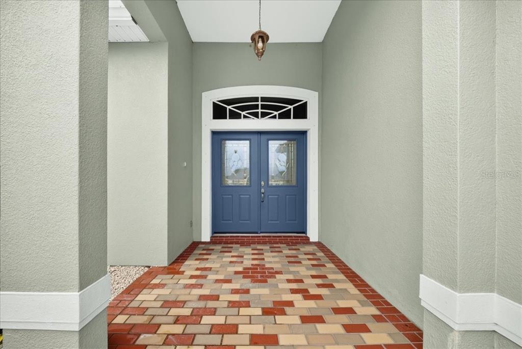 A covered entryway features a blue double door with glass inserts and a brick paver floor — 6463 FLORA VISTA PLACE, COCOA, FL