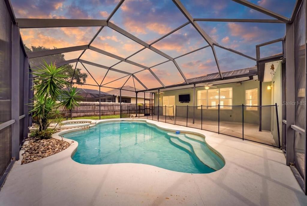 A screened-in swimming pool with a rock garden and patio area at sunset — 6463 FLORA VISTA PLACE, COCOA, FL