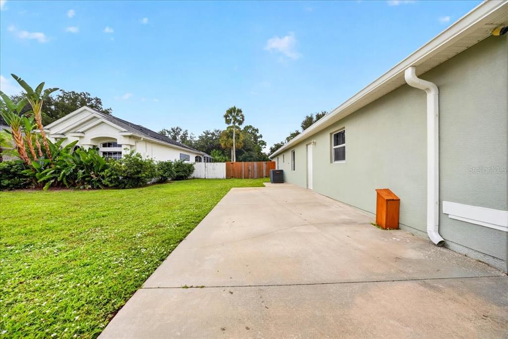 A concrete patio extends along the side of a light green house with a lawn — 6463 FLORA VISTA PLACE, COCOA, FL