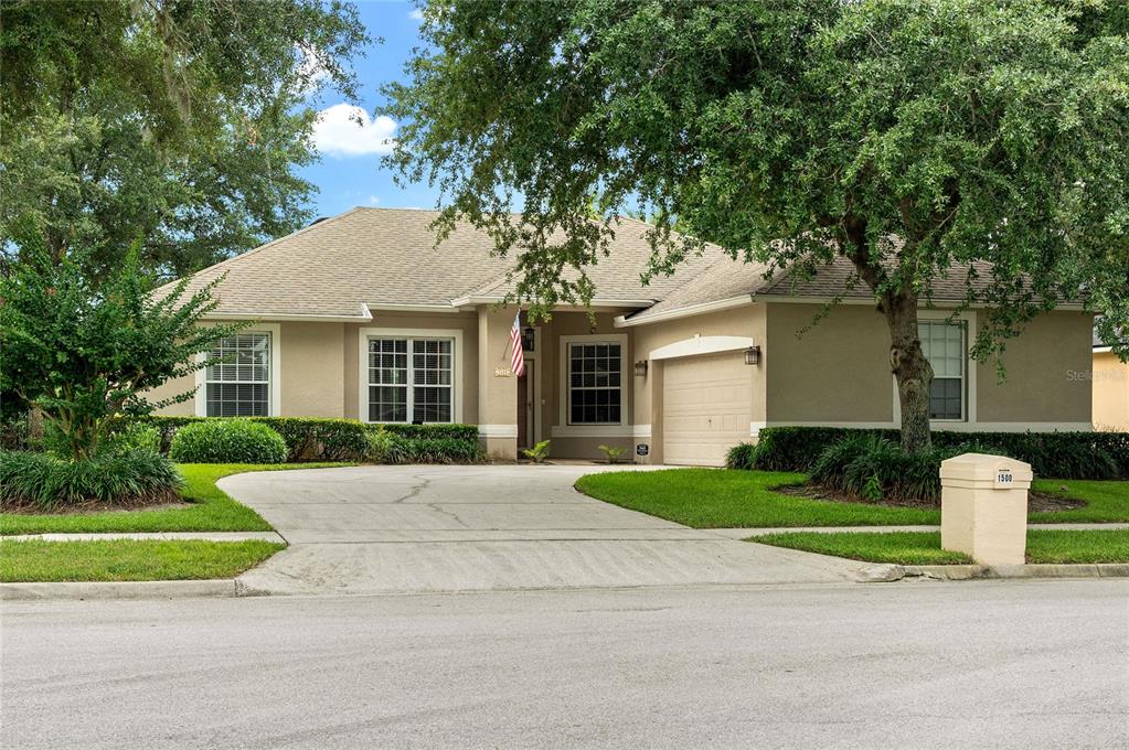A single-story house with a beige exterior, a concrete driveway, and a large front tree — 1500 LUCKY PENNIE WAY, APOPKA, FL