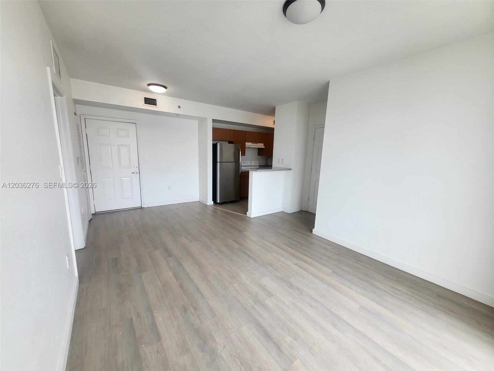 An open-concept living area features light wood-look flooring, white walls, and a small kitchen — 120 SW 8th Ave # 703, Miami FL 33130, MIAMI, FL