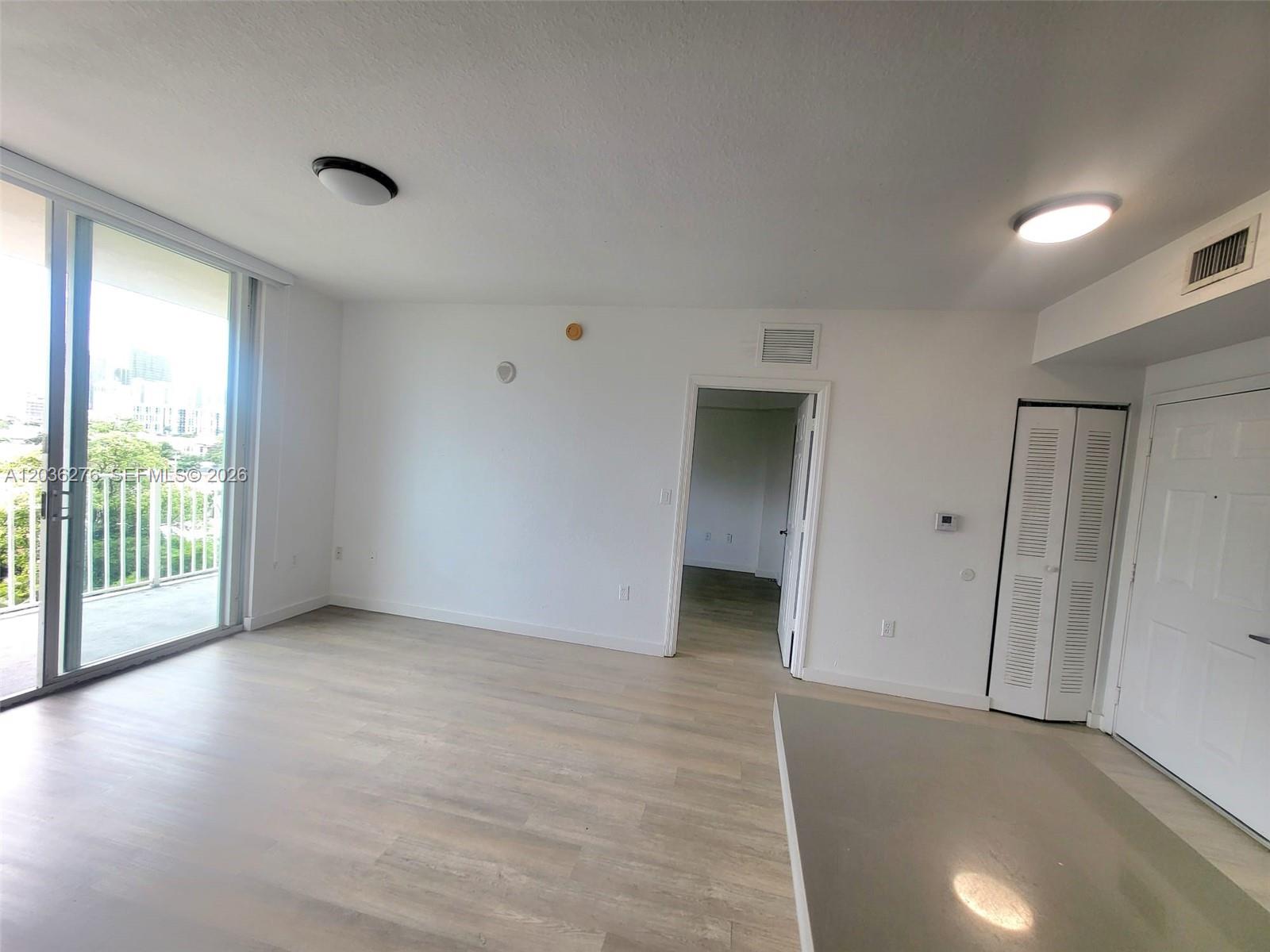 An empty living room features light wood-look flooring, white walls, a balcony, and a closet — 120 SW 8th Ave # 703, Miami FL 33130, MIAMI, FL