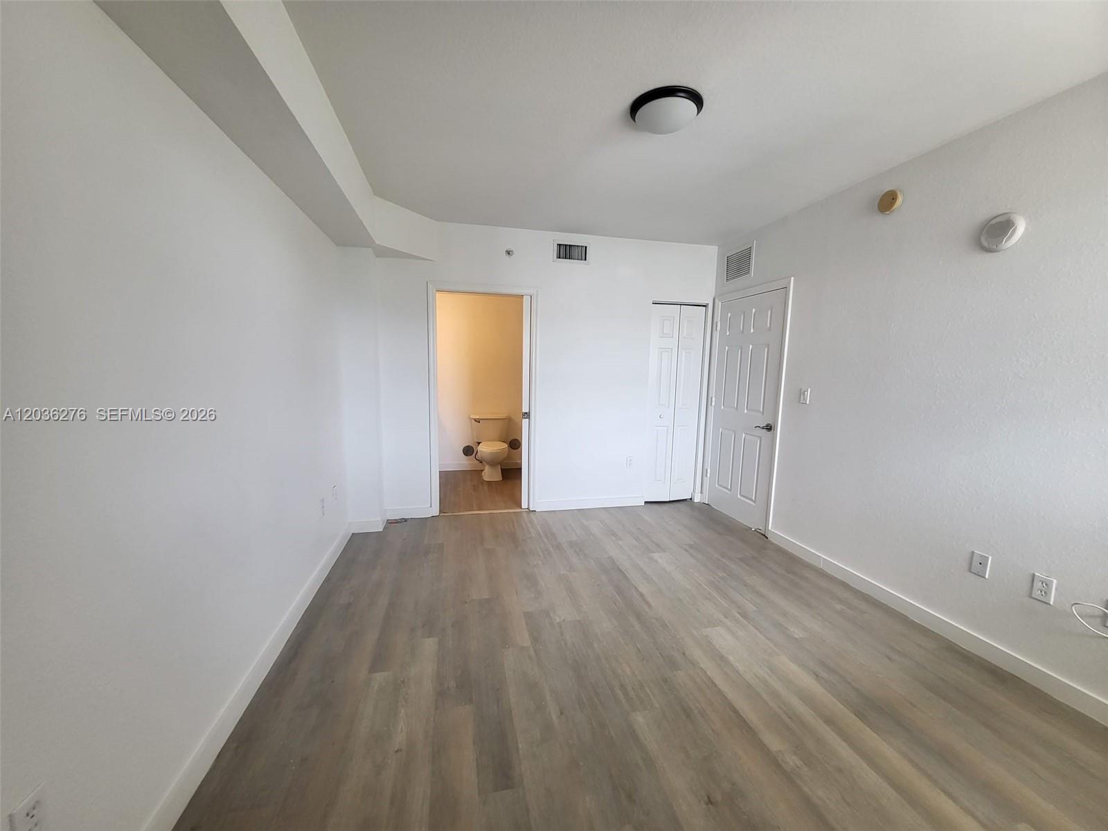 An empty room with light wood-look flooring, white walls, a closet, and an attached bathroom — 120 SW 8th Ave # 703, Miami FL 33130, MIAMI, FL