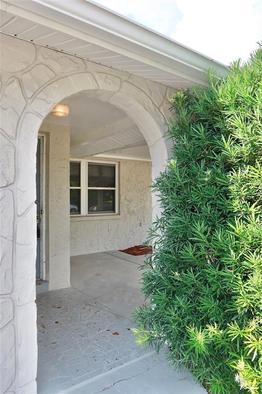 A covered entryway features a stone-textured arched opening, a light fixture, and a nearby bush — 6533 RIDGE CREST DRIVE, PORT RICHEY, FL