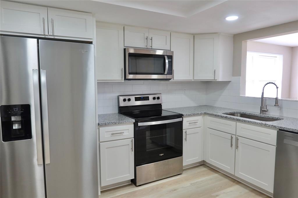 A modern kitchen features white cabinets, stainless steel appliances, and gray speckled granite countertops — 6533 RIDGE CREST DRIVE, PORT RICHEY, FL