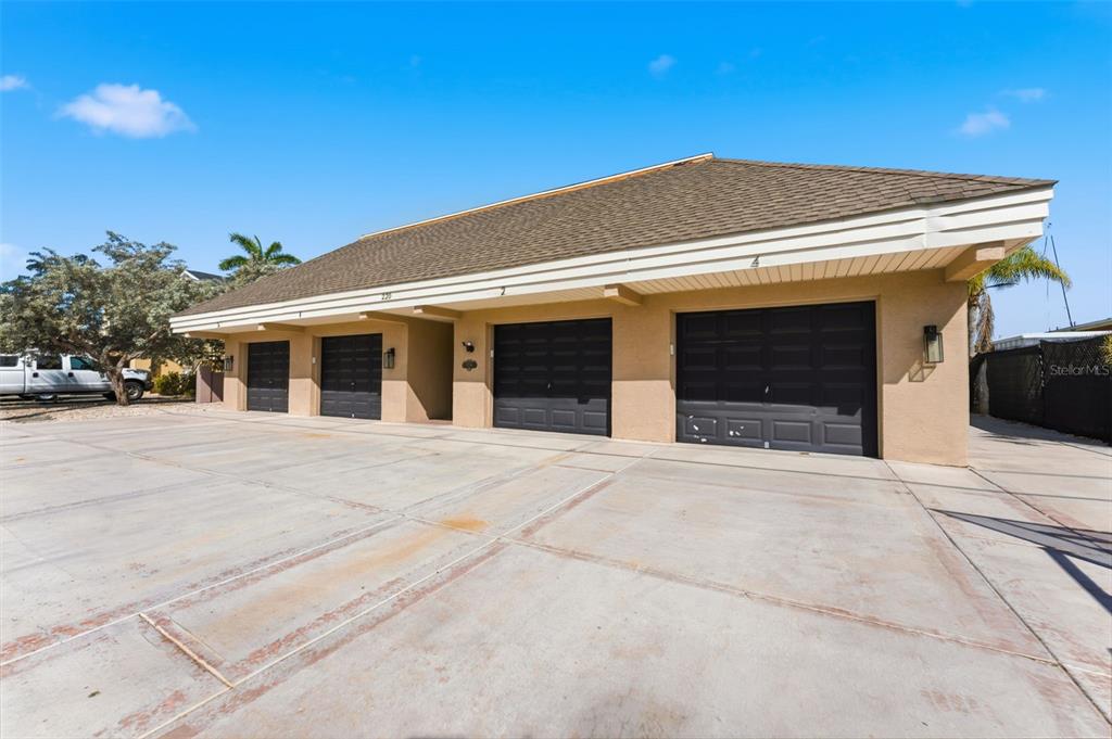 A multi-unit garage building features four dark doors and a concrete driveway under a blue sky — 220 126TH AVENUE UNIT 1, TREASURE ISLAND, FL