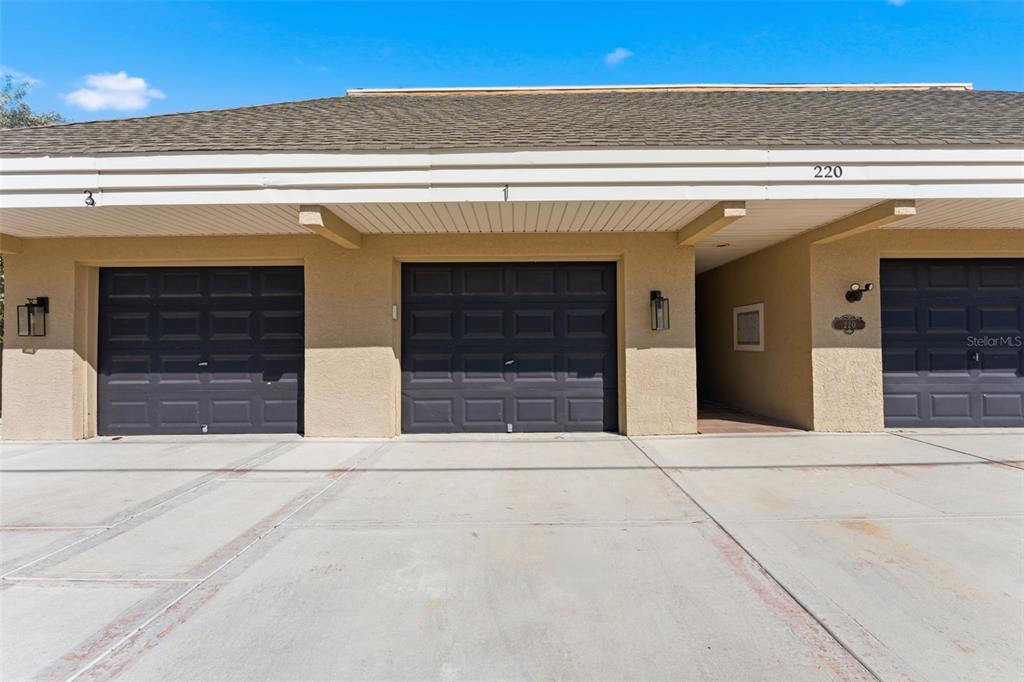 A row of three garage doors with tan stucco walls and a shingled roof — 220 126TH AVENUE UNIT 1, TREASURE ISLAND, FL