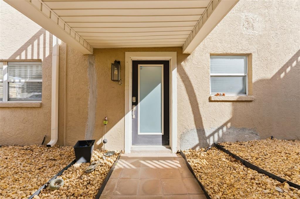 The exterior of a home features a covered entryway with a modern glass-paneled front door — 220 126TH AVENUE UNIT 1, TREASURE ISLAND, FL