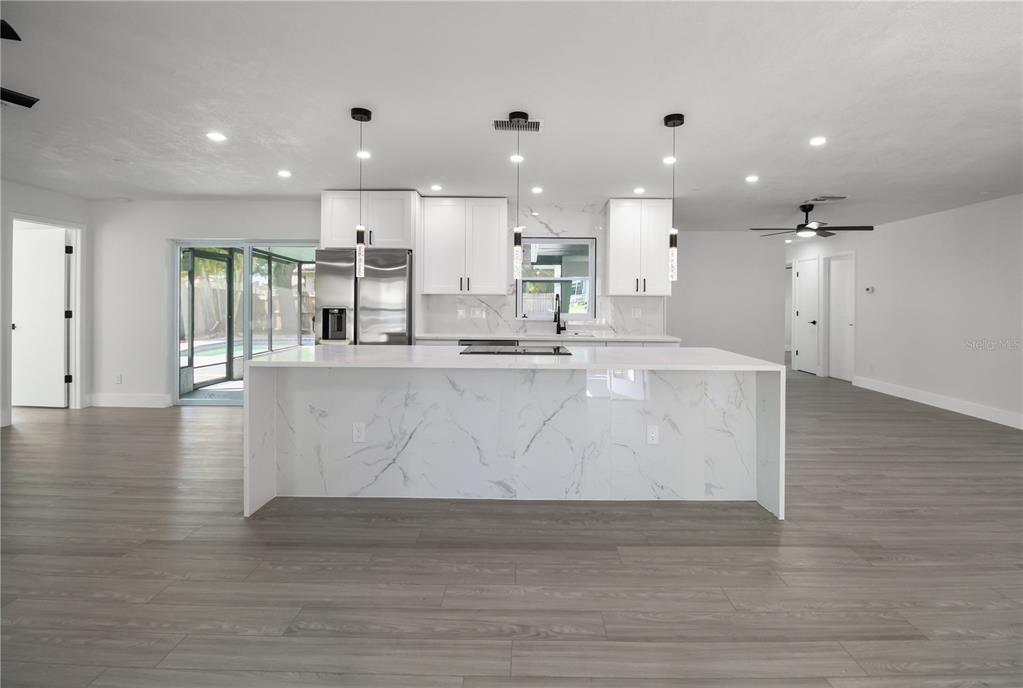 A modern kitchen features white cabinets, a marble-topped island, and wood-look flooring — 11492 93RD STREET, LARGO, FL