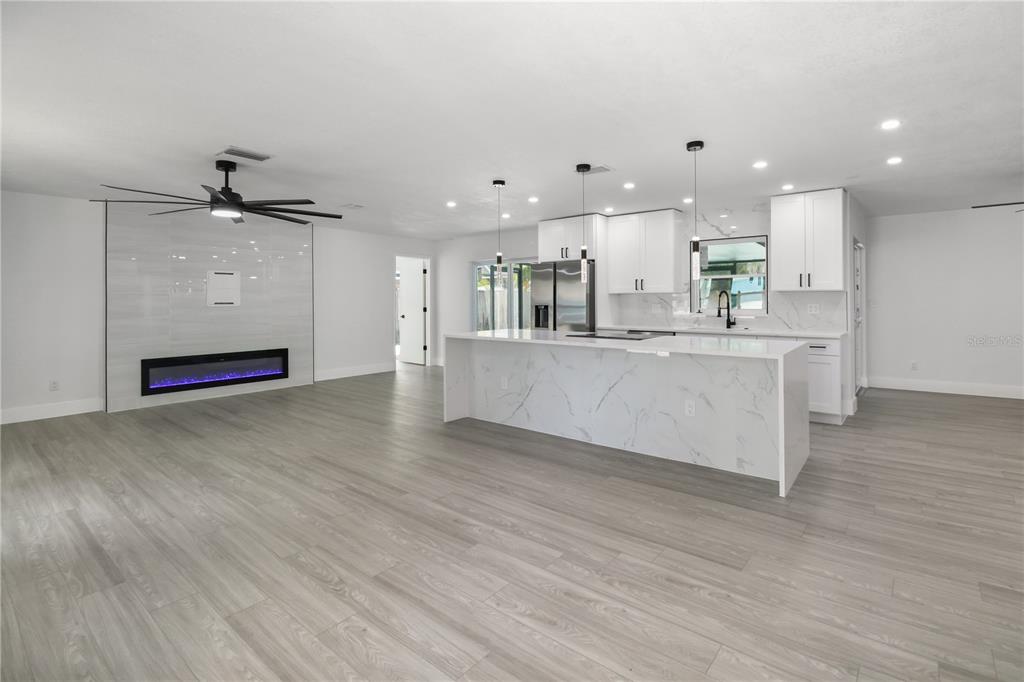 A modern open-concept kitchen and living area featuring a marble island and electric fireplace — 11492 93RD STREET, LARGO, FL