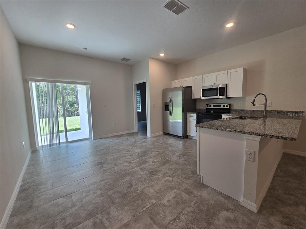 An open-concept kitchen and dining area features tile flooring, stainless steel appliances, and sliding doors — 2025 DUNBAR ST UNIT 2025, BARTOW, FL