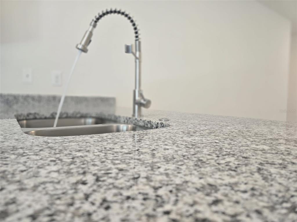 A kitchen island features a granite countertop and a stainless steel pull-down faucet — 2025 DUNBAR ST UNIT 2025, BARTOW, FL