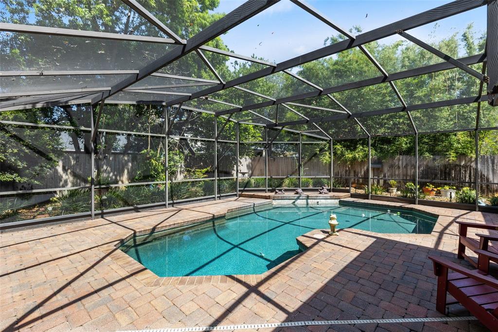 A screened-in swimming pool with a brick paver deck and a wooden fence background — 553 ARAPAHO TRAIL, MAITLAND, FL