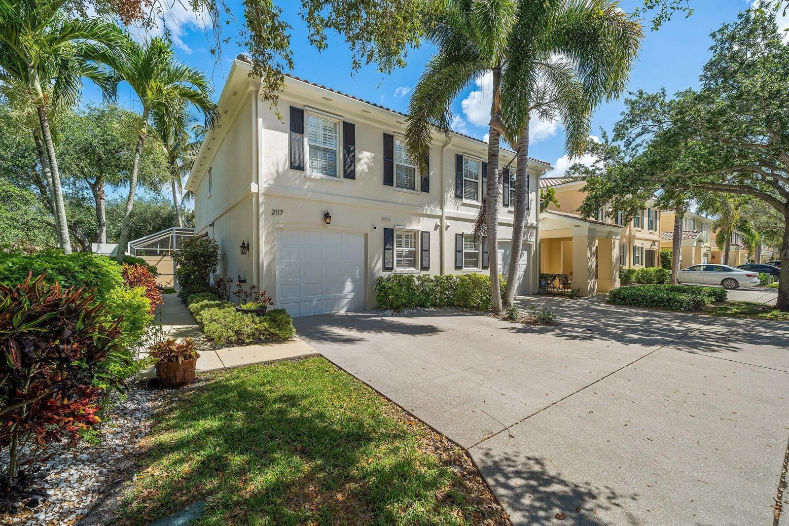 A two-story stucco townhouse with black shutters, a garage, and a palm tree out front — 2117 Tigris Drive, West Palm Beach FL 33411, WEST PALM BEACH, FL