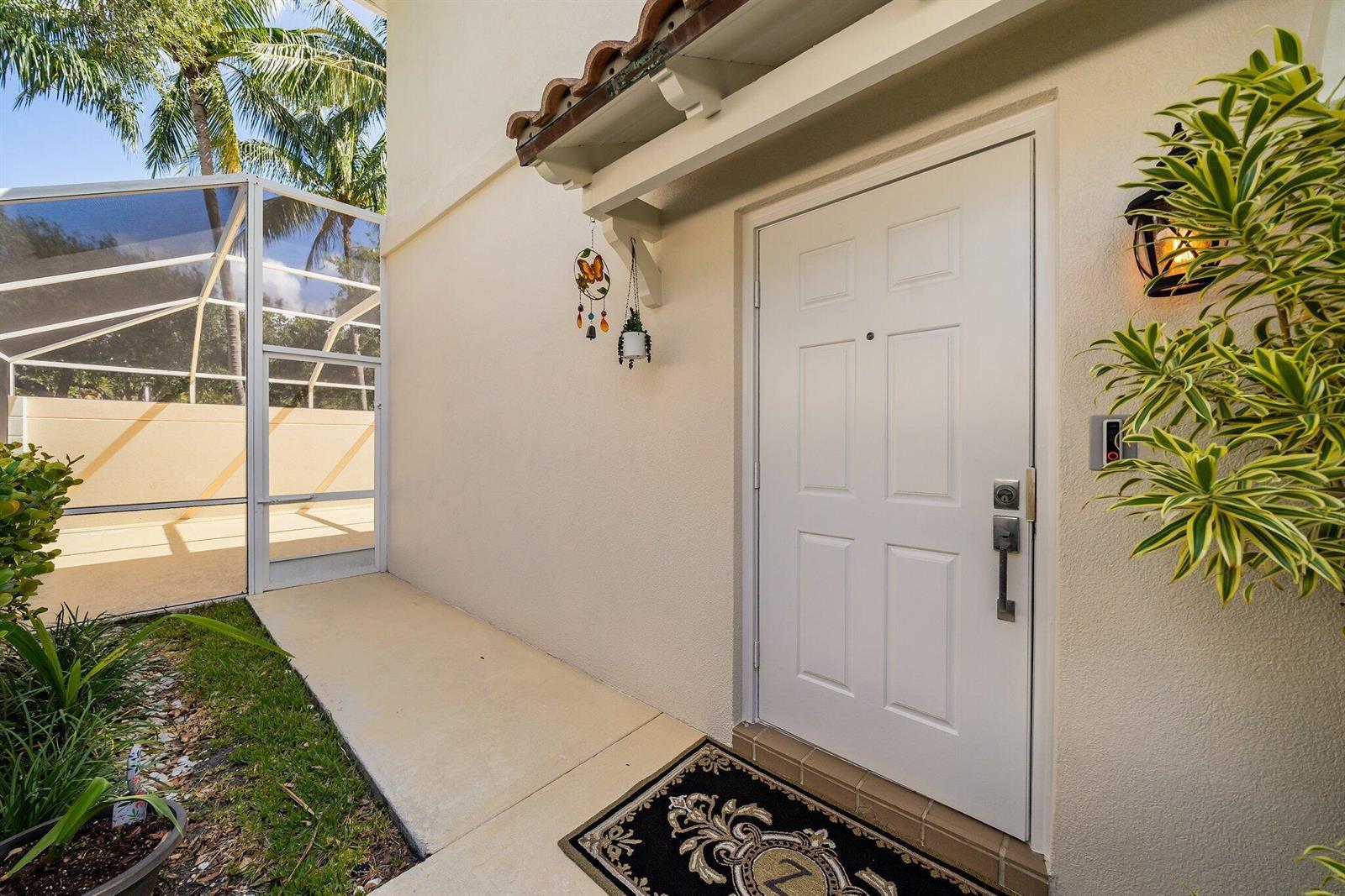 A white front door with a decorative mat sits under a small roof overhang — 2117 Tigris Drive, West Palm Beach FL 33411, WEST PALM BEACH, FL
