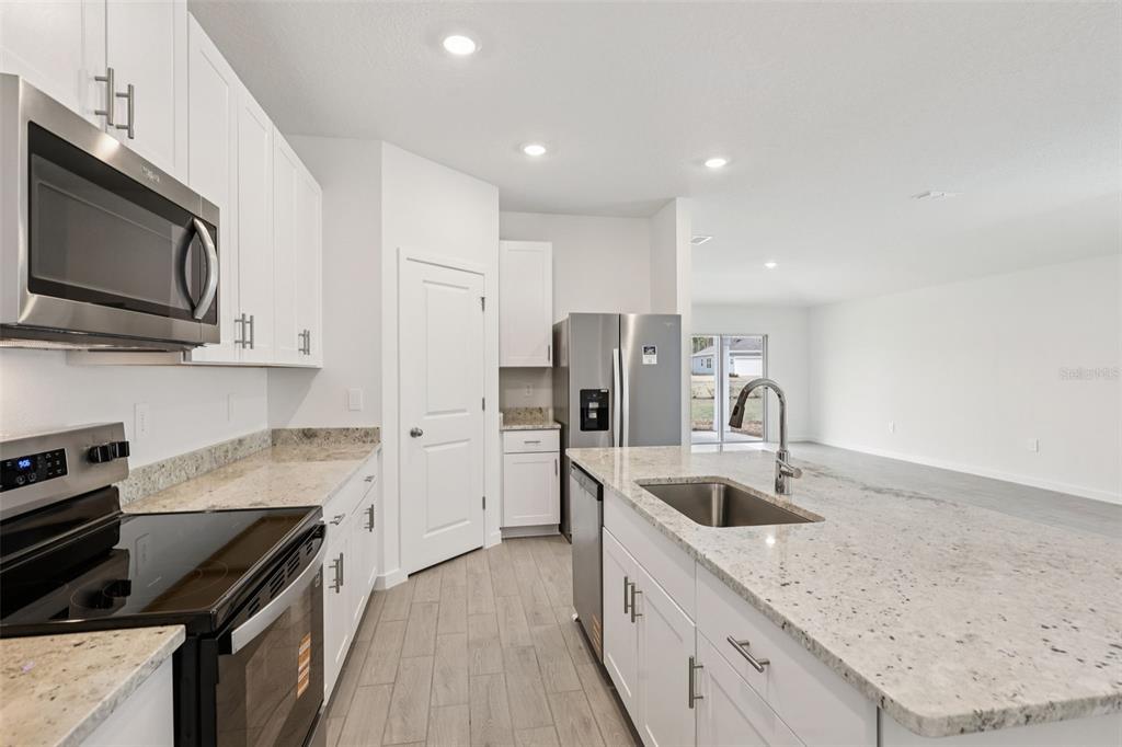 A modern kitchen features white cabinets, granite countertops, stainless steel appliances, and light wood flooring — 71 WANDERING CREEK WAY, PALM COAST, FL