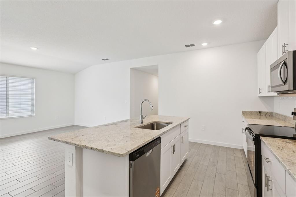 A kitchen features white cabinets, granite countertops, a center island with a sink, and tile flooring — 71 WANDERING CREEK WAY, PALM COAST, FL
