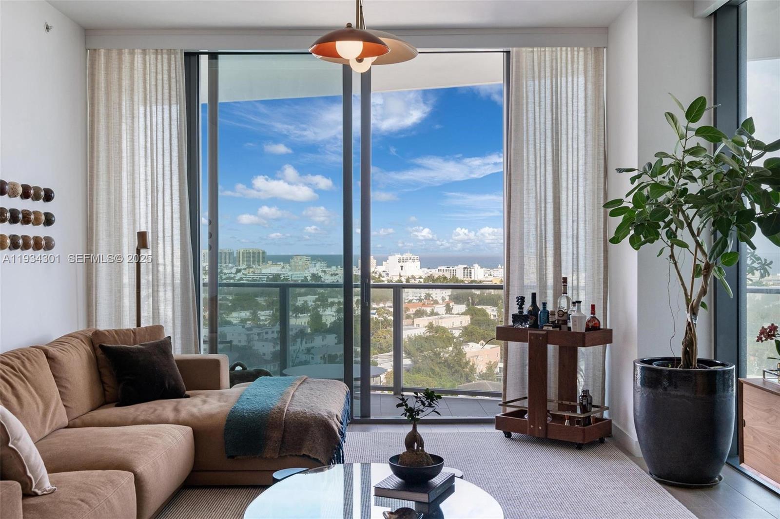 A living room features a tan sectional sofa, a bar cart, and floor-to-ceiling windows overlooking a city — 500 Alton Rd # 1602, Miami Beach FL 33139, MIAMI BEACH, FL