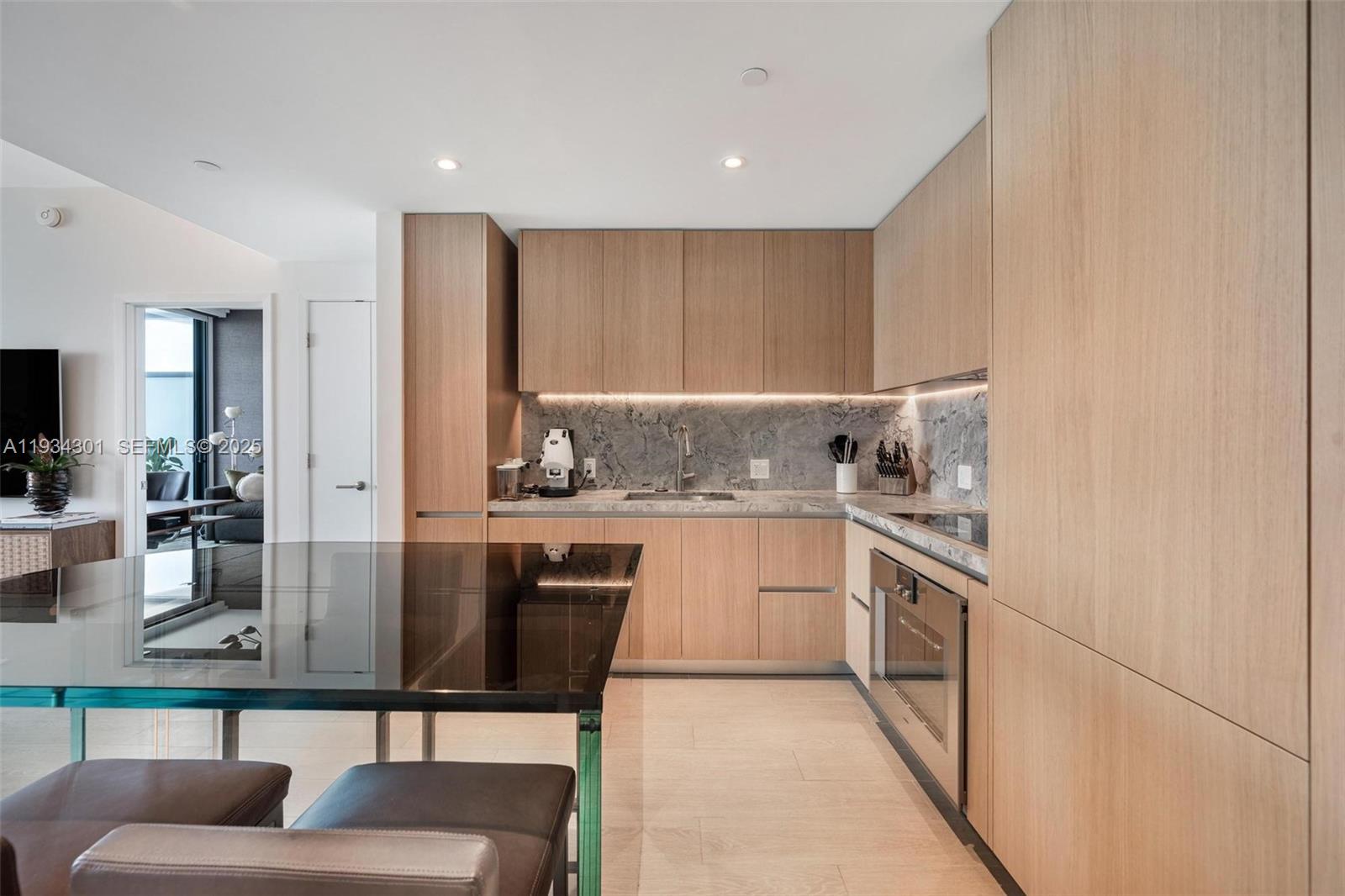 A modern kitchen features light wood cabinetry, a marble backsplash, and a glass-topped island — 500 Alton Rd # 1602, Miami Beach FL 33139, MIAMI BEACH, FL