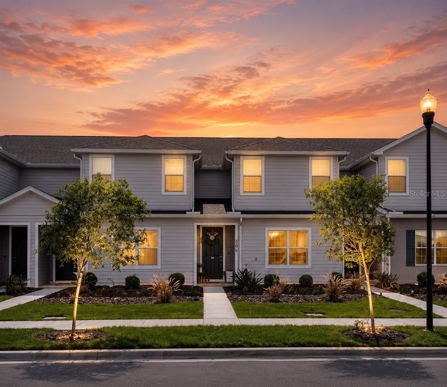 A two-story townhouse exterior features light gray siding, a dark front door, and two trees — 380 HUCKLEBERRY BLOSSOM DRIVE, ST CLOUD, FL