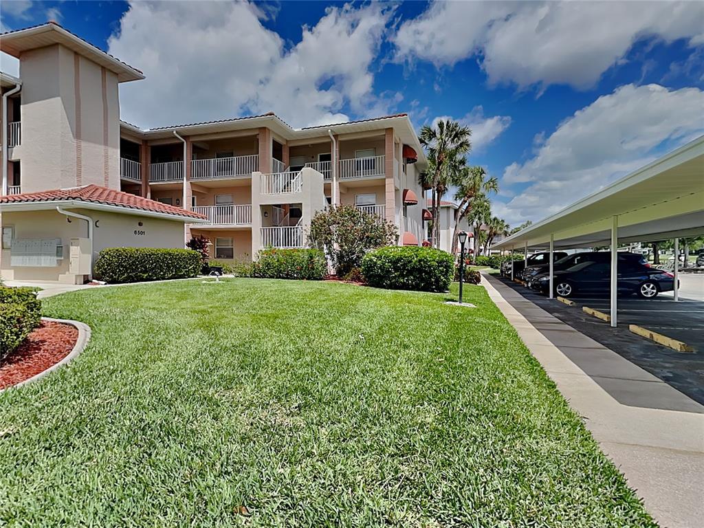 A three-story apartment building with a grassy lawn and a covered parking area — 6501 STONE RIVER ROAD UNIT 110, BRADENTON, FL