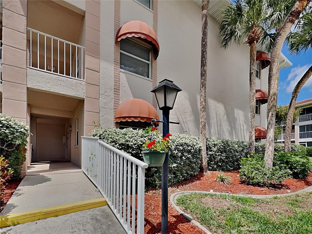 An exterior view of a multi-story apartment building with a ramp and red awnings — 6501 STONE RIVER ROAD UNIT 110, BRADENTON, FL
