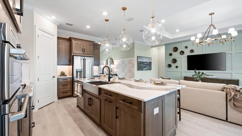 A modern kitchen features wood cabinetry, a large marble-topped island, and pendant lighting — 11221 CARDING MILL LANE, WINTER GARDEN, FL
